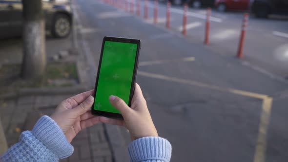Girl Uses a Phone with a Green Screen on the Street. Scrolling Pages