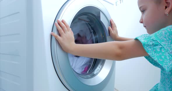 Cute Child Looks Inside the Washing Machine. Cylinder Spinning Machine. Concept Laundry Washing alt