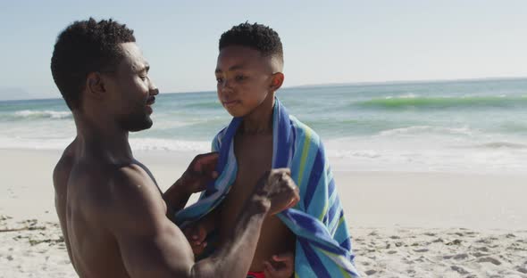 Smiling african american father toweling off his son on sunny beach alt