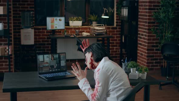Angry Creepy Office Zombie Sitting at Desk While Gesturing Angrily at Digital Video Call alt