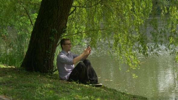 Man Sitting Near the Water With Mobile Phone