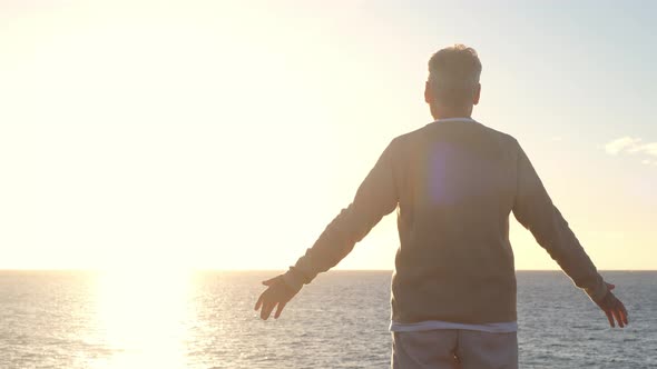 old man looking to the sunset and the sea with opened arms feeling free and happy - freedom