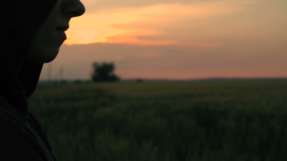 Profile Of Man In Hood On The Sunset In The Field Background alt