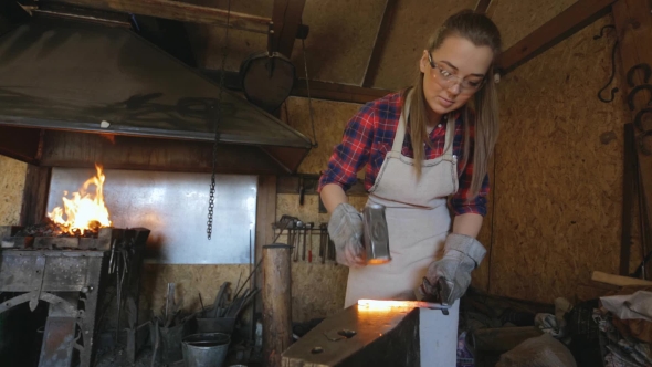 Woman Blacksmith Strikes Hammer On Hot Metal Workpiece. alt