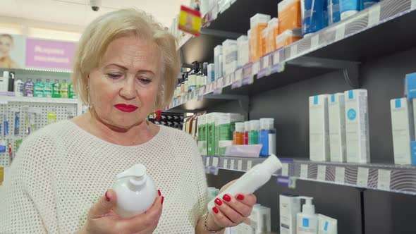 Lovely Senior Woman Smiling, Choosing Between Two Products at the Drugstore alt