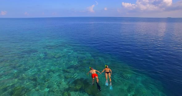 Aerial drone view of a man and woman couple snorkeling over the coral reef of a tropical island. alt
