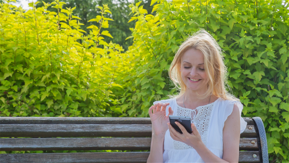 Happy Smiling Girl Using a Smartphone in a City Park Sitting on a Bench 4