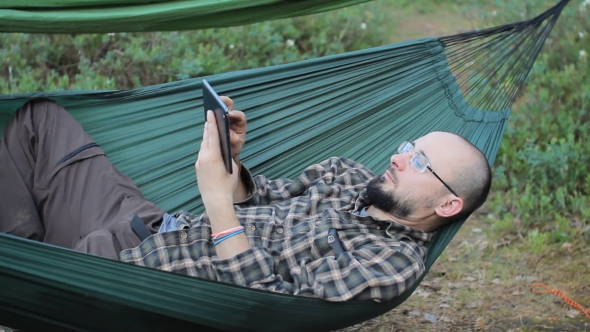 A Man In a Hammock Is Video Calling On The Tablet. 