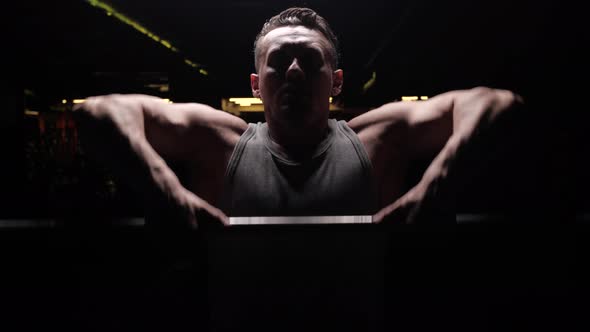 Silhouette of a Sports Man with Relief Muscles on the Background of a Dark Gym