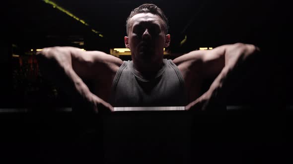 Silhouette of a Sports Man with Relief Muscles on the Background of a Dark Gym alt
