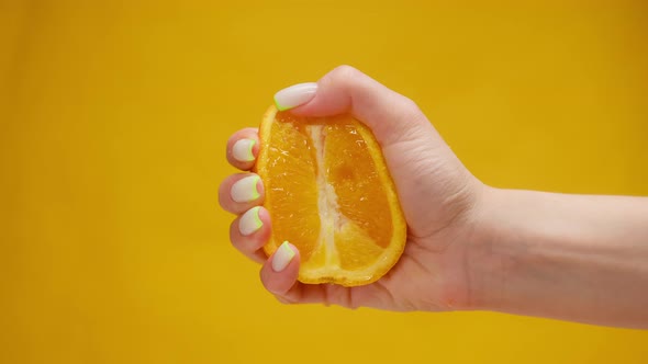 Closeup of Squeezing Orange Juice with Splashes By Female Hand on Orange Background Making Citrus alt