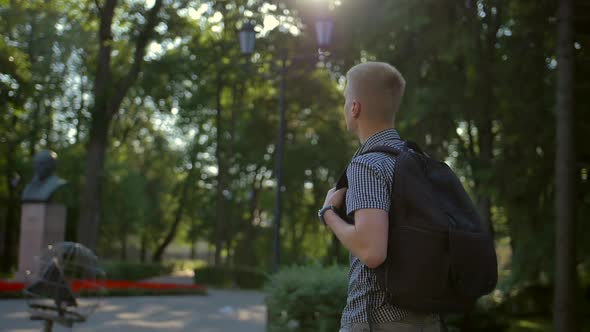 Side View of a Student Photographer Is Walking Along a European Town Street Behind Him alt