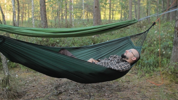 A Man In a Hammock Touch Smartwatch. Man In The Woods With a Beard And Glasses