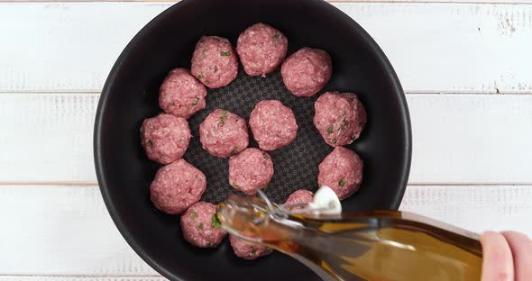 Pouring olive oil on raw meatballs