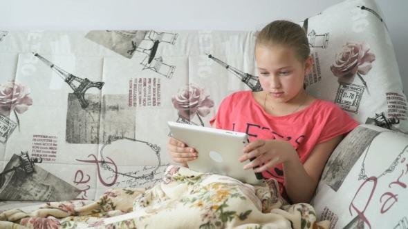 Teenager Girl Uses a Digital Tablet On The Bed