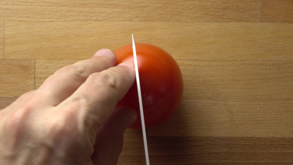Man Splitting Whole Red Tomato On The Wooden Cutting Board alt