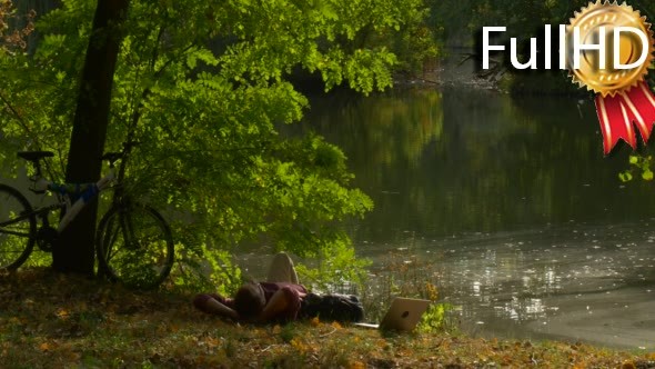 Man is Sitting at Lake Bank Working With Laptop alt