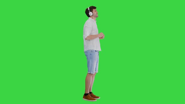 Casual Young Man in Headphones Listening To Music and Enjoying It on a Green Screen, Chroma Key. alt