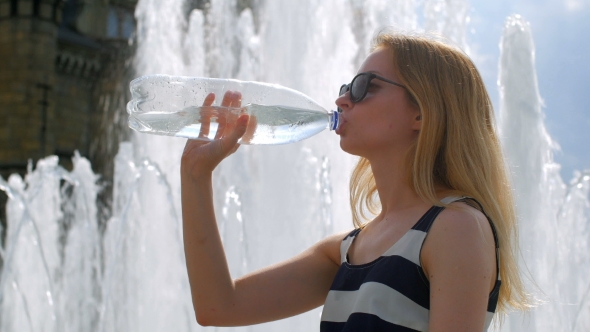 Blonde In Sunglasses Drinks Water From Bottle Sitting Half-turned On a Fountain