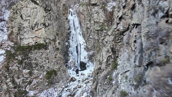 Narrow Mountain Waterfall Surrounded By Rocks and Snow