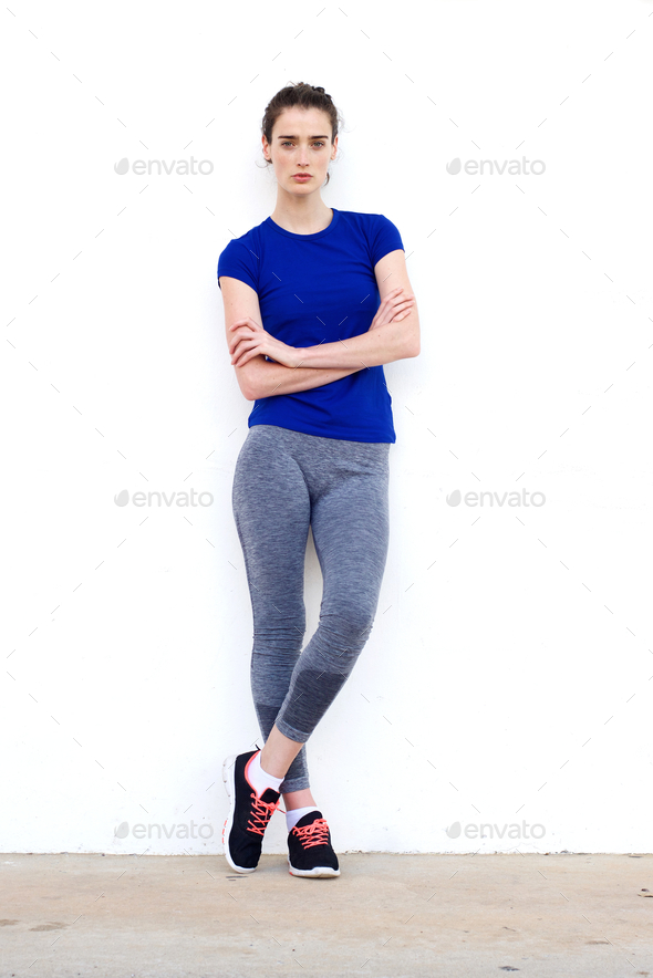Sporty Woman Leaning Against White Wall With Arms Crossed Stock Photo
