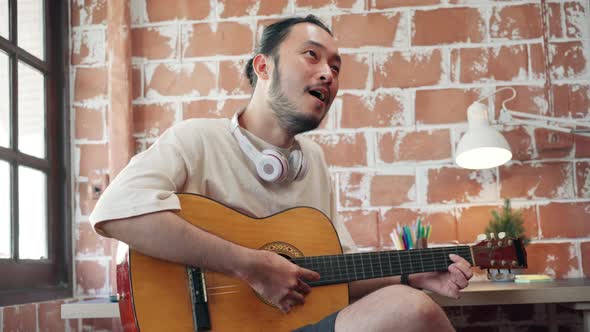 Artists producing music in their home sound studio, Asian man playing guitar and singing. alt