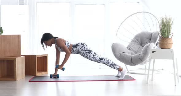 Black woman doing fitness at home with dumbbells.