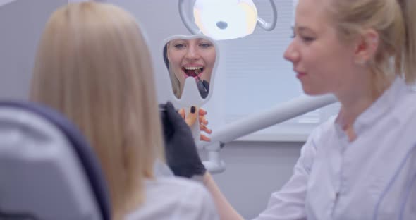 Nice Girl Patient Is Looking at How Her Tooth Was Filled in the Mirror. Satisfied Patient Looks in alt