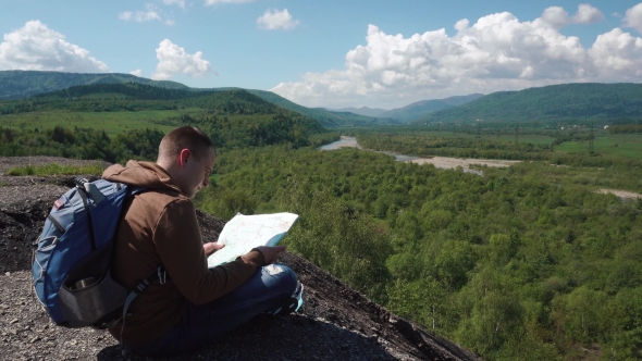 Young Active Man Checking Landscape Terrain With Map While Sitting on Mountain Rock