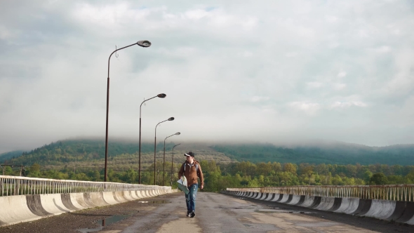 Young Male Tourist Checking His Way On Route With Map When Walking On Empty Highway In Mountains