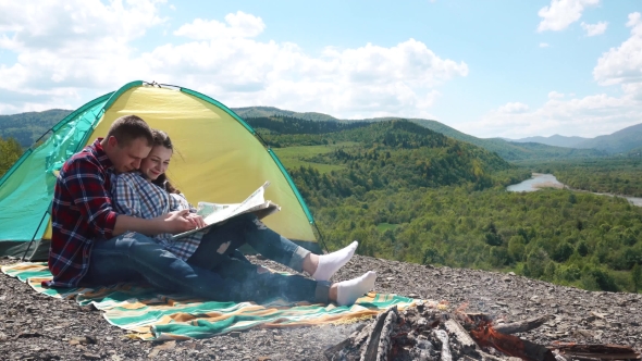 Young Tourist Couple Have a Sensual Moment Sitting In Camping. Beautiful Young Man Holds And Kisses