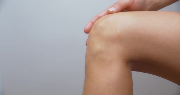 Naked woman applying cream on her knee and caressing her skin.Isolated shot. alt