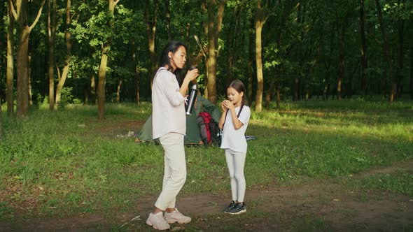 Happy Asian Woman Enjoys Vacation with Her Daughter Walking Along the Forest Path Drinking Tea From alt