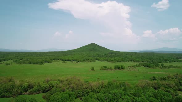 Aerial View of an Endless Geen Meadow and a Hill Against the Blue Sky with Clouds alt