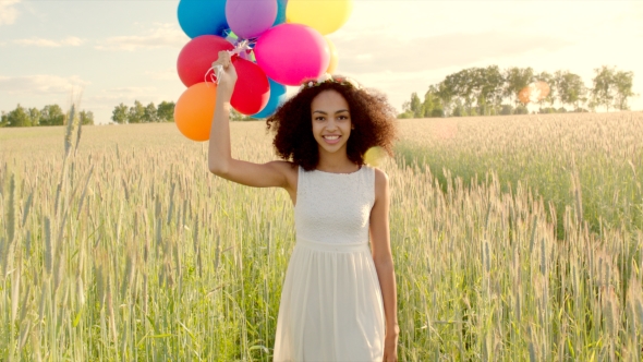 Young Girl Walking Through a Wheat Field With Colour Balloons During Sunset alt