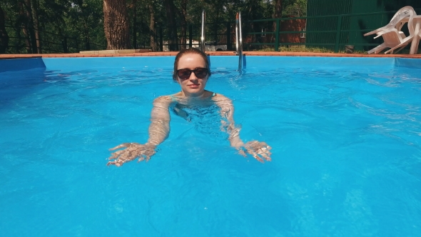 Blonde Dressed In Light Blue Swimsuit And Sunglasses Is Swimming In a Pool