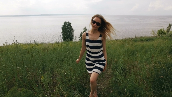 Young Smiling Blonde In Sunglasses Is Walking On a Field In Windy Wheather