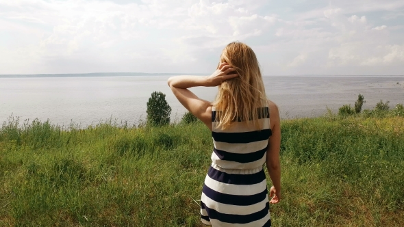 Blonde Is Walking On a Field In Sunny Weather,back View,sea On Background