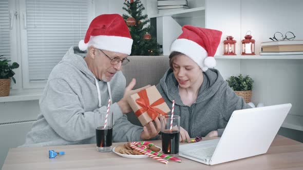 An Elderly Father and a Teenage Son in Santa Claus Hats and with a Gift Box in Their Hands