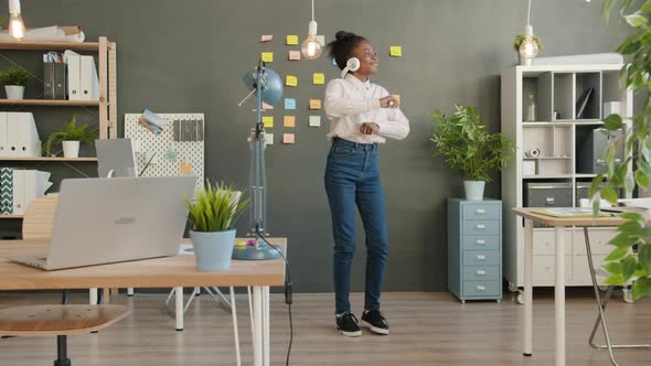 Joyful African American Businesswoman in Headphones Dancing in Creative Office Partying Alone alt