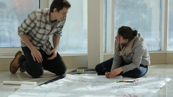 Two Persons Sit On Floor And Discuss Plan Of Building alt
