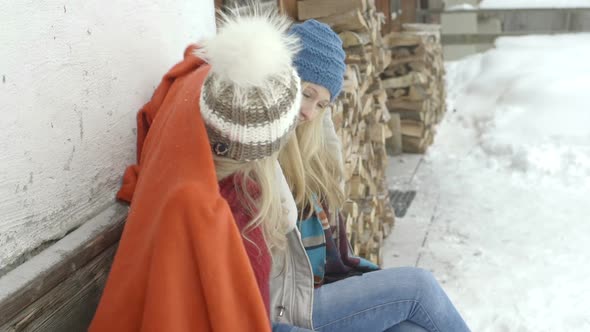 Young women sitting outside chalet and sharing blanket