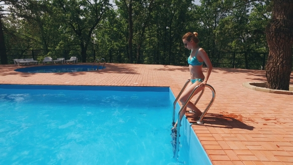Woman Dressed In Light Blue Swimsuit Is Going Into Pool Outdoor And Swimming