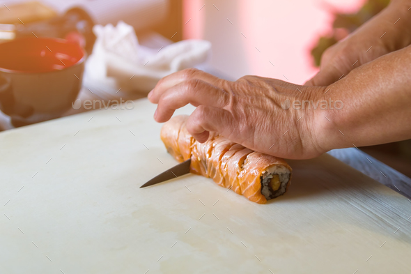 Hands with knife cut sushi.