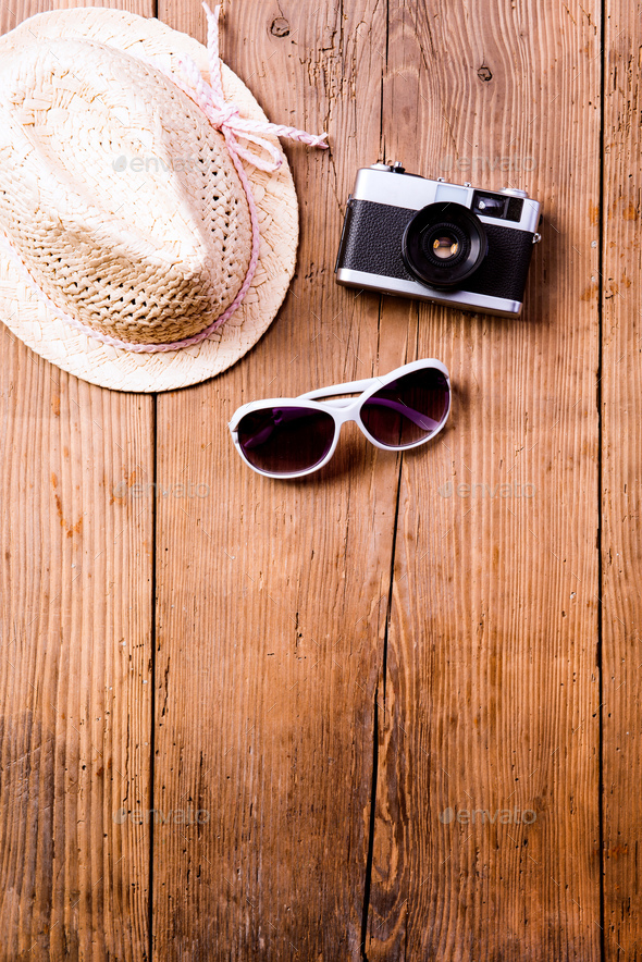 Sunglasses, hat and vintage camera against wooden background.