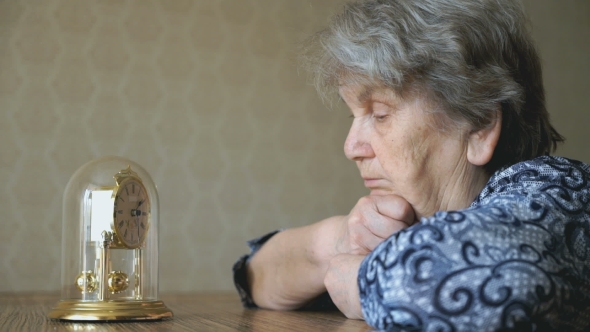 Old Woman Looks At The Table Clock With Pendulum