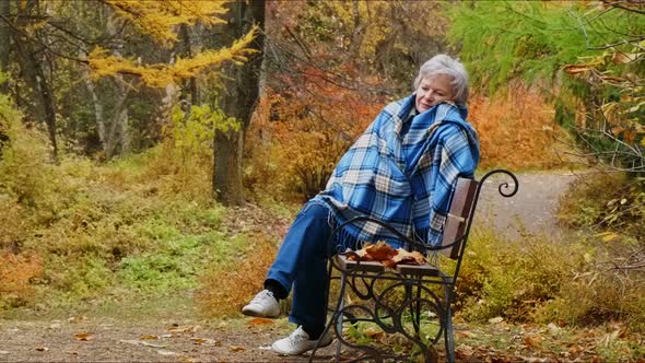Elderly Woman Walks in the Park in Autumn and Relaxes. alt