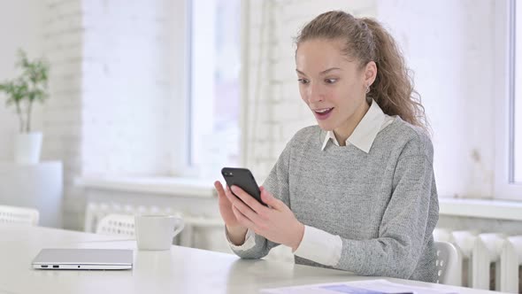 Young Latin Woman Celebrating Success on Smartphone alt