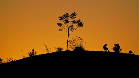 Silhouette of a Guy Sitting on the Rounded Hill During Sunset