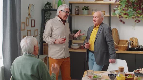 Senior Men Chatting over Wine by Dinner Table alt